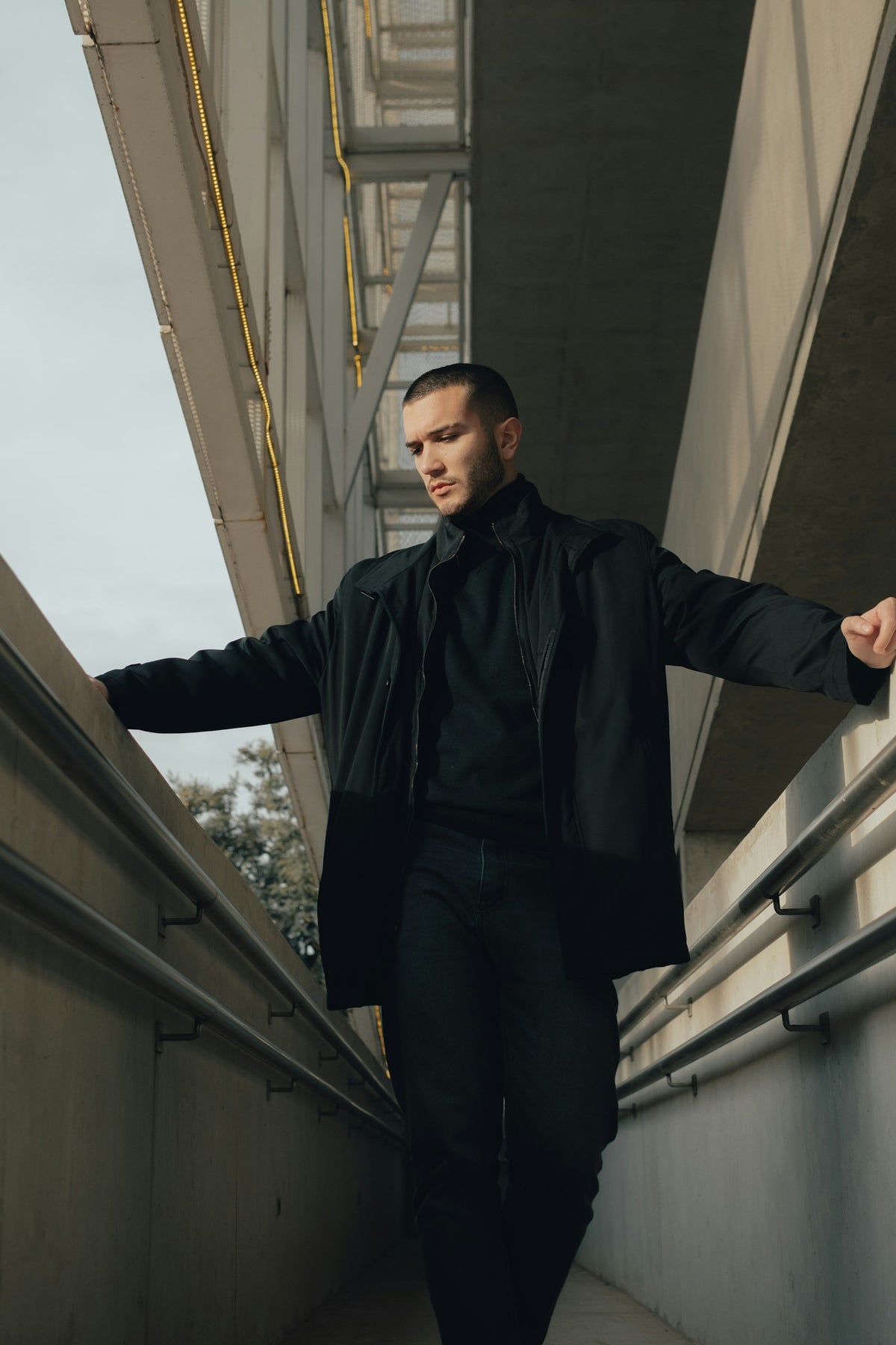 Man in a black jacket walking along a concrete bridge